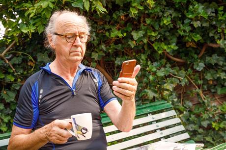 Meneer kijkt op zijn telefoon terwijl hij koffie drinkt op een bankje